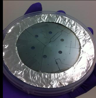 Figure 3: A four inch PTFE wafer, with a metal mask,
      showing deep-etched microfluidic ducts (top). Fine detail of the
      microfluidic duct system on this wafer is also shown (bottom).